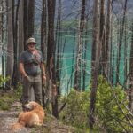 Man hiking on a trail with his dog and a kenai