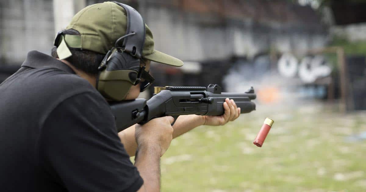 Man wearing protective ear muffs while firing shotgunn