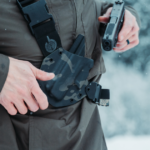 A man in the snow checking the holster retention of his GunfightersINC Kenai Chest Holster.