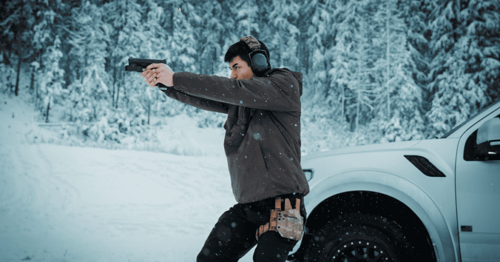 A man outdoors in the snow shooting his gun wearing a GunfightersINC holster.