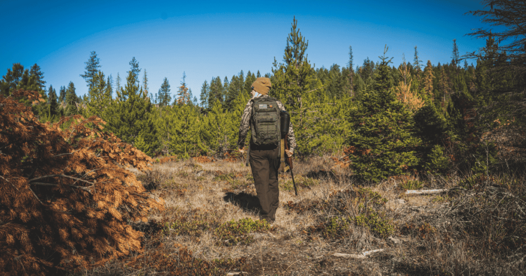 A woman carrying bear hunting gear walking in the forest.