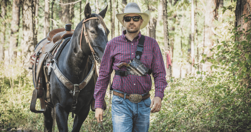 A man wearing a chest holster by GunfightersINC and walking his horse.