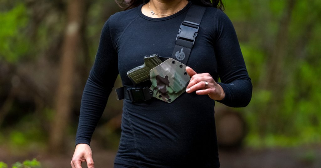 A woman in black trail running with a GunfightersINC Kenai chest holster.