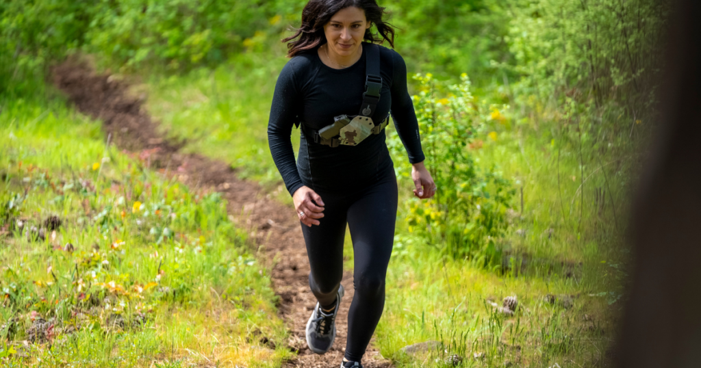 A woman trail running with a Kenai Chest Holster by GunfightersINC.