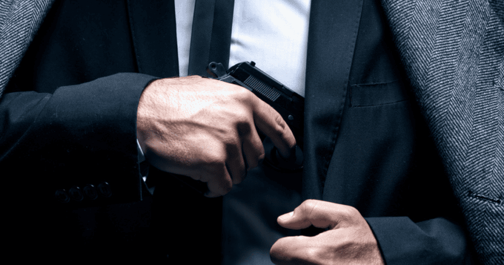 A man in a suit putting his concealed carry gun into his shoulder hoslter.