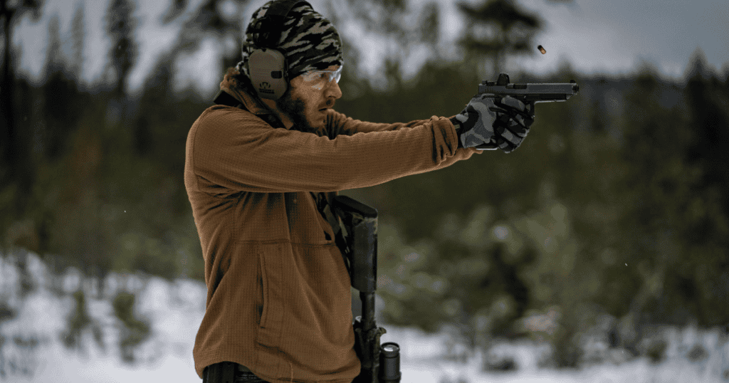 A man shooting his gun in the snow to work on managing recoil.