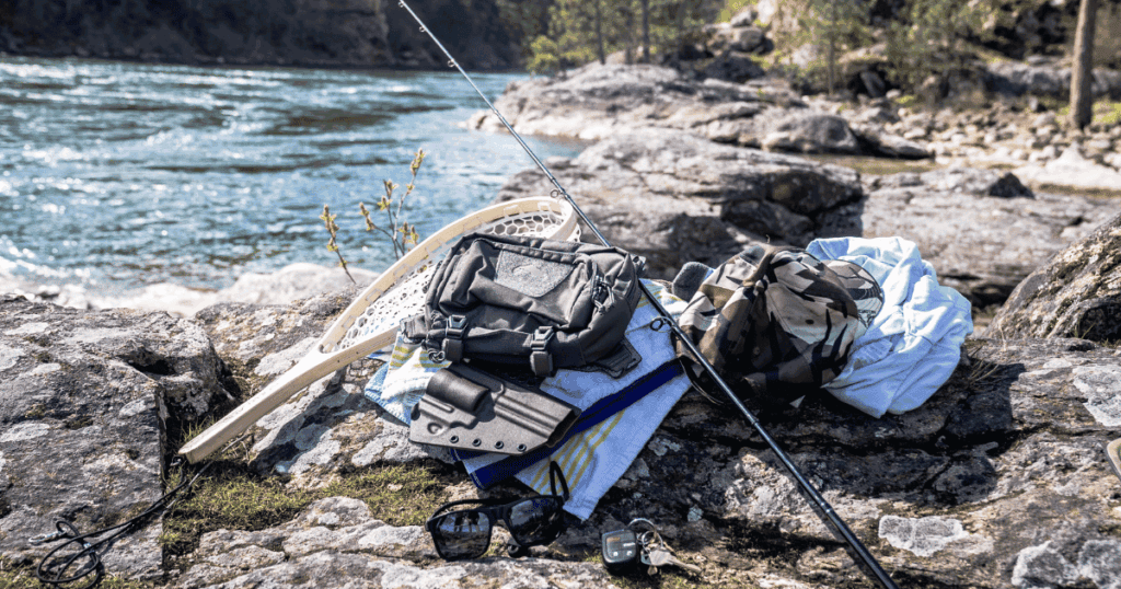 The GunfightersINC Tackle Link Holster connected to a tackle chest pack laying on rocks next to a river.