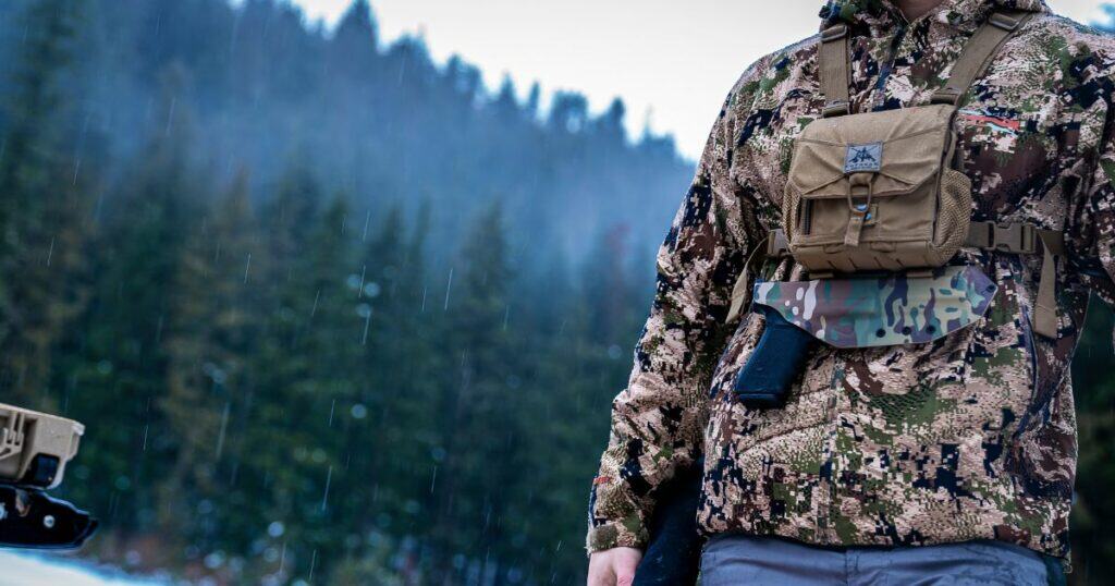 A hunter in camo wearing a GunfightersINC Bino-Link Holster while it's snowing.