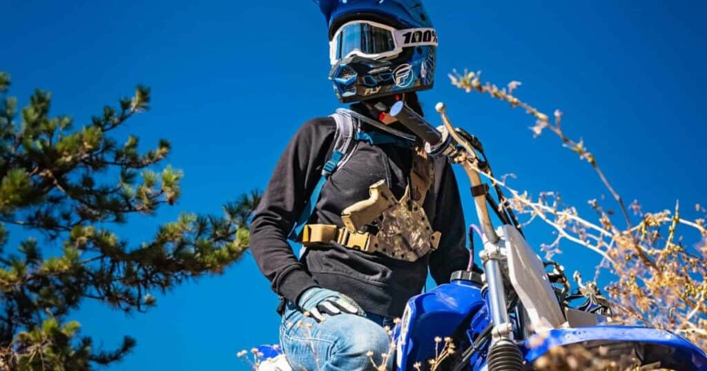 A man on a motor bike wearing a GunfightersINC Kenai Chest Holster.