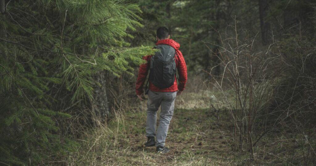 A man in a red jacket carrying a backpack hiking through the backcountry.