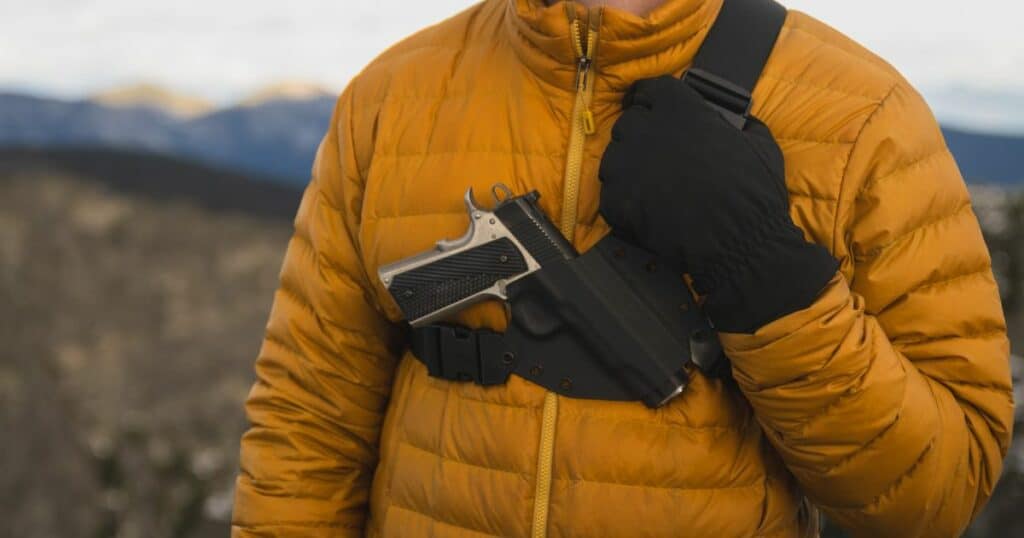 A man hiking in a yellow jacket wearing the GunfightersINC Kenai Chest Holster.