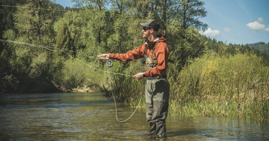 A man fly fishing wearing waders and a GunfightersINC Kenai Chest Holster.