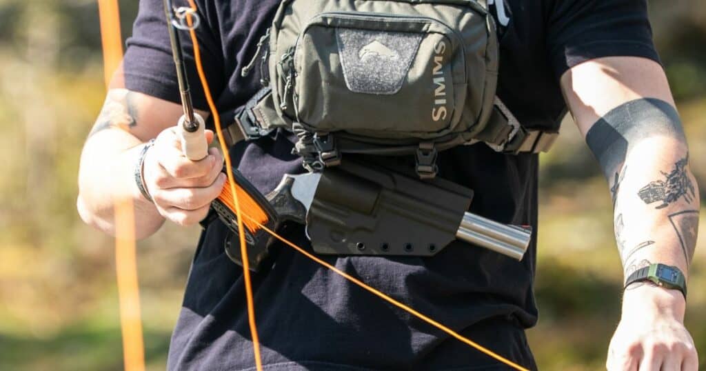 A man fly fishing wearing a GunfightersINC Tackle Link Holster to carry his gun.