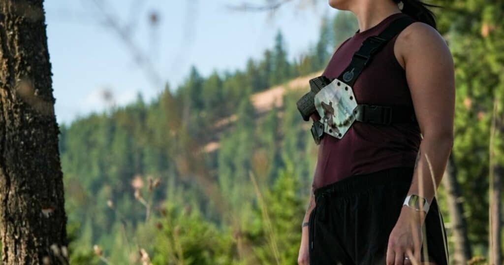 A woman trail running wearing a GunfightersINC Kenai Chest Holster.