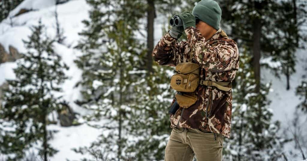 A man wearing a GunfightersINC Bino-Link Holster while hiking to his next ice fishing spot.