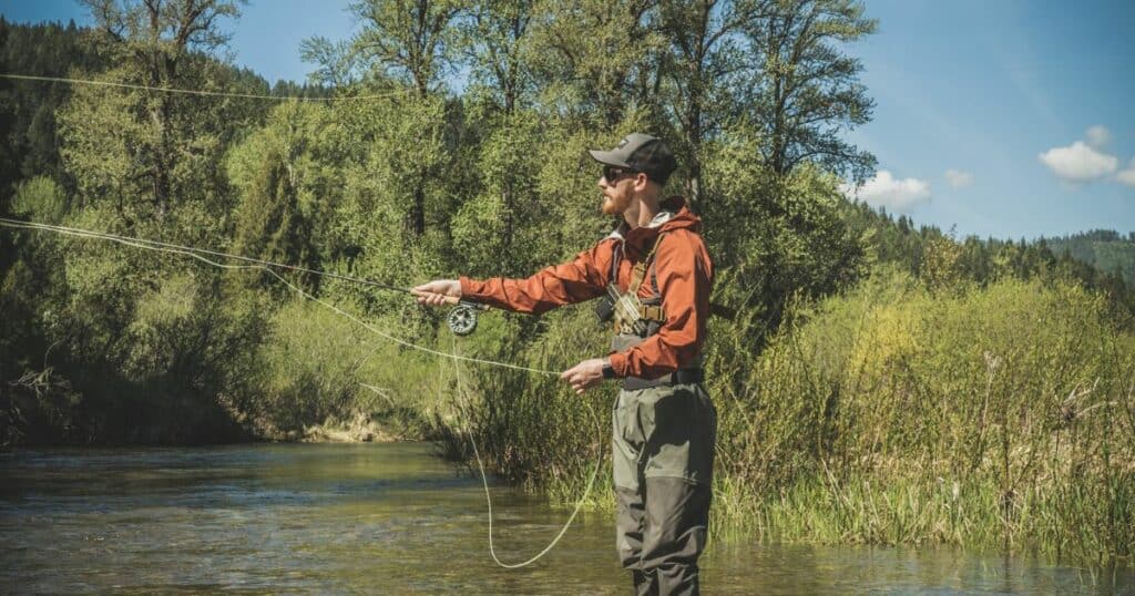 A man is fly fishing in a river wearing a chest holster from GunfightersINC.