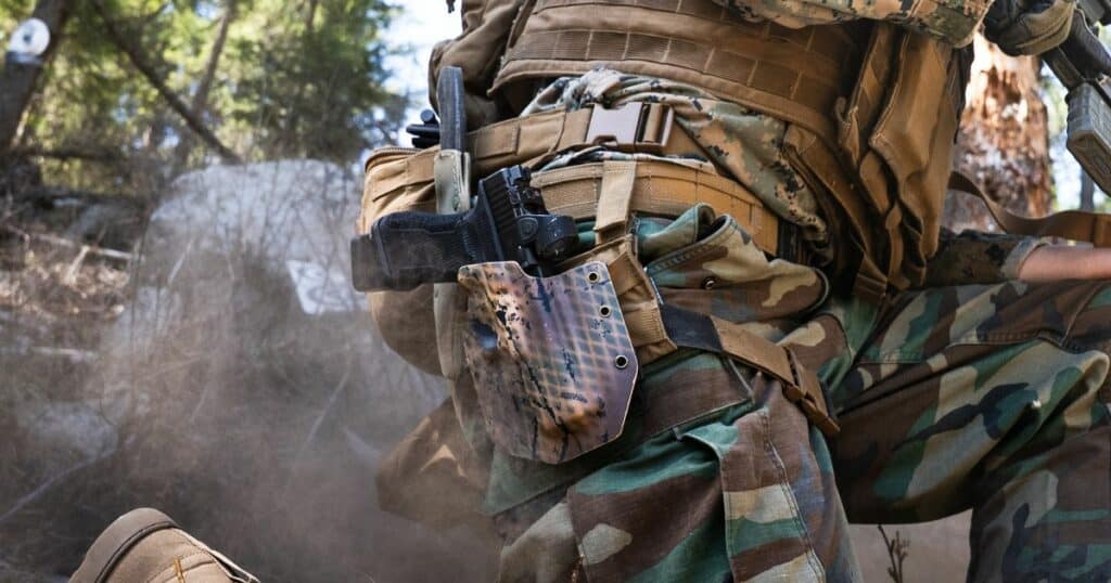 A man kneeling and shooting while wearing a GunfightersINC holster.