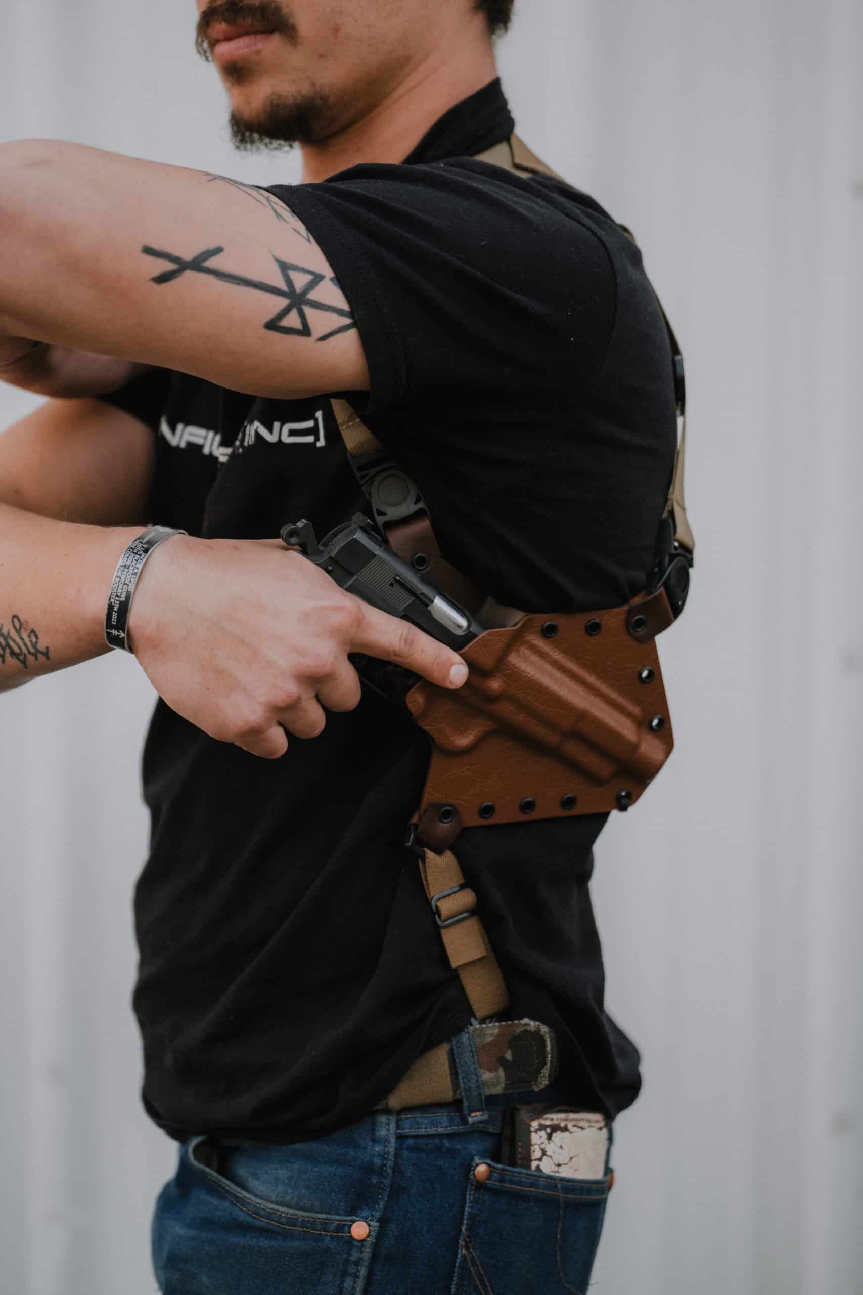 A man with tattoos removing his pistol from his Spectre Shoulder Holster.