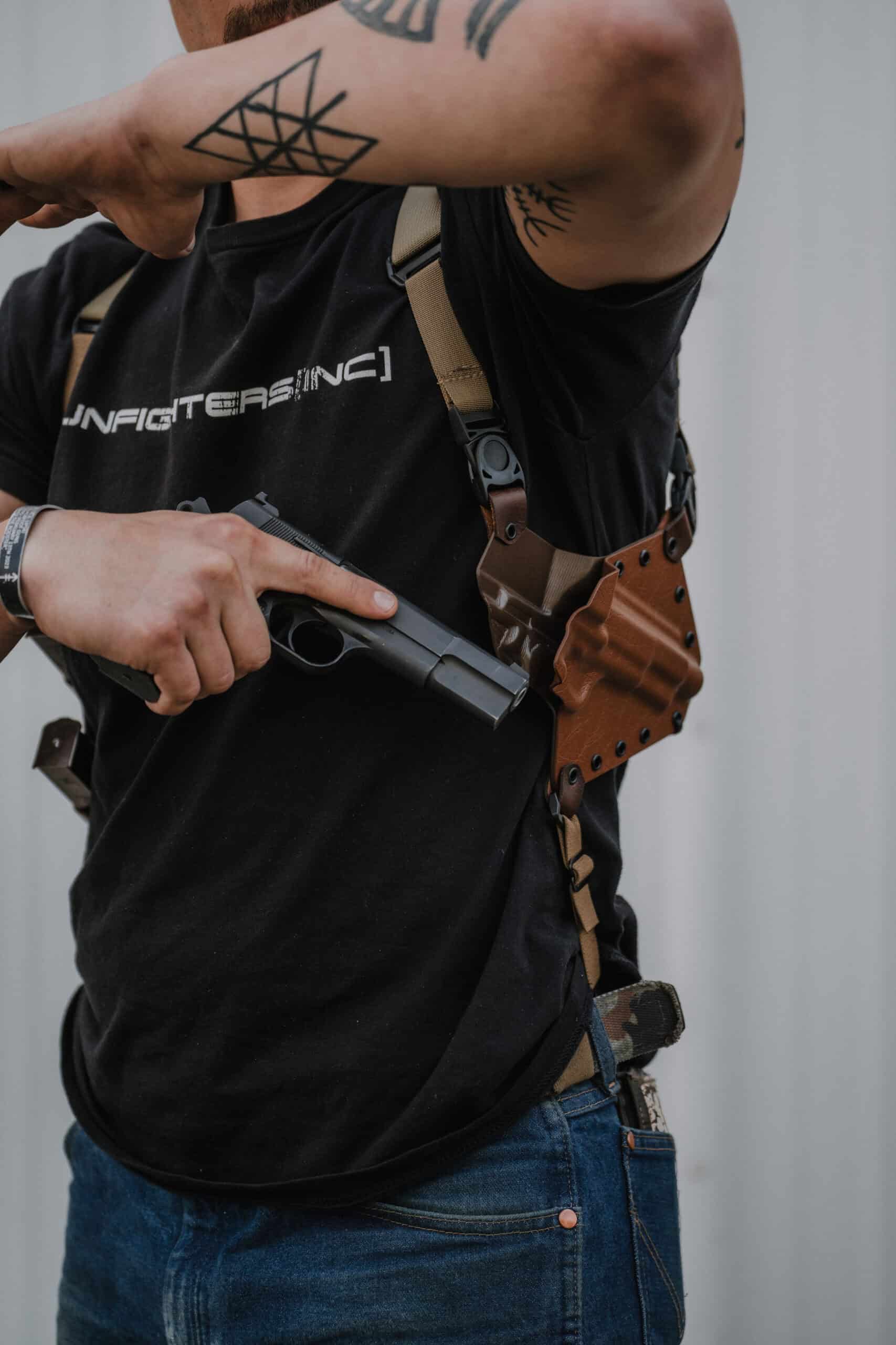 A man in a GunfightersINC t-shirt removing his pistol from his Spectre Shoulder Holster.