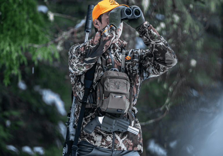 A man using his binoculars carrying a bino harness with a pistol holster attached.