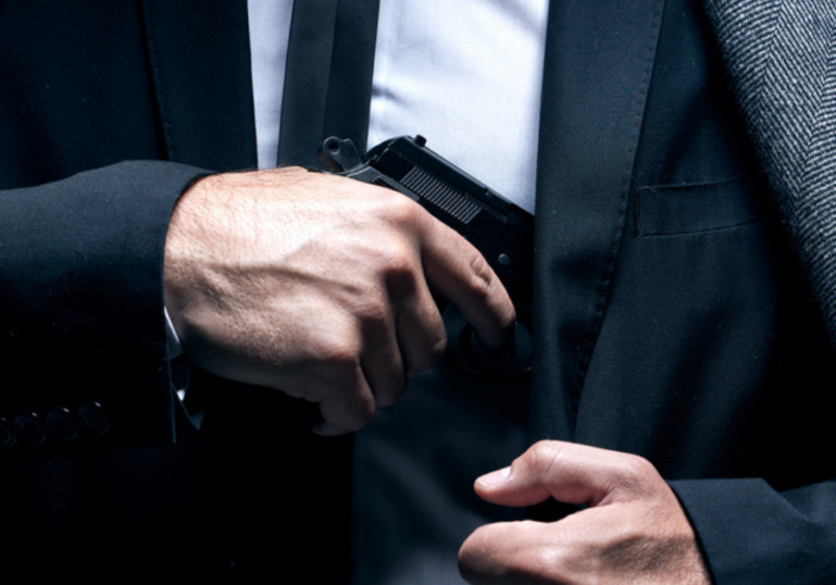 A man in a suit putting his concealed carry gun into his shoulder hoslter.