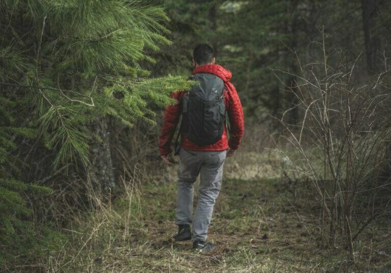 A man in a red jacket carrying a backpack hiking through the backcountry.