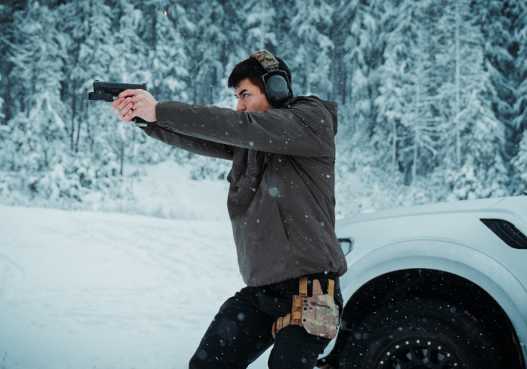 A man outdoors in the snow shooting his gun wearing a GunfightersINC holster.