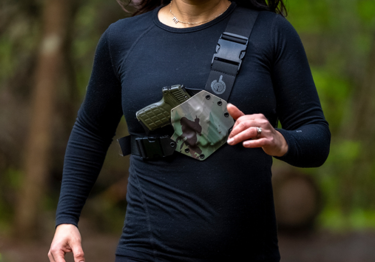 A woman in black trail running with a GunfightersINC Kenai chest holster.