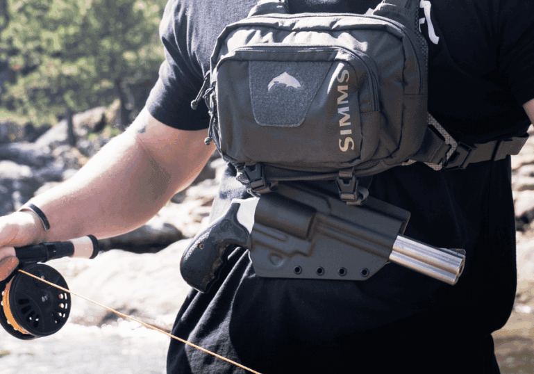 A man casting his rod while wearing a tackle chest pack and holster.