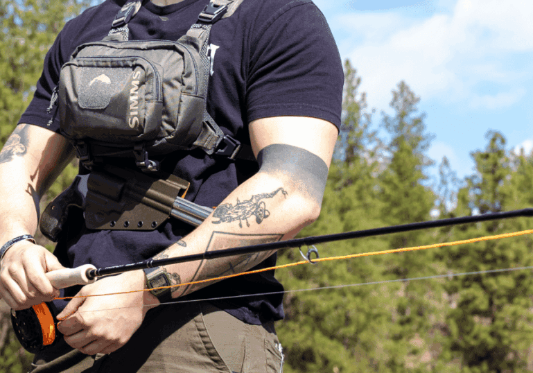 A man out fishing wearing a chest pack with a Tackle Link Holster from GunfightersINC attached.